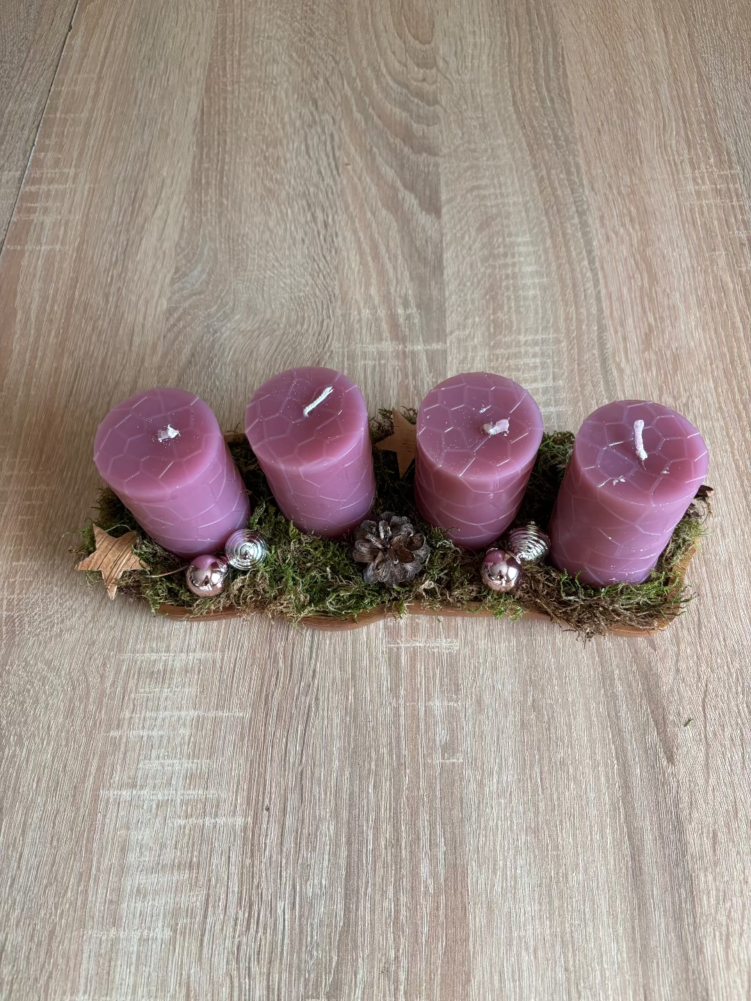 Länglicher Adventskranz mit runden rosa Kerzen, geschmückt mit Moos, Christbaumkugel und Tannenzapfen
