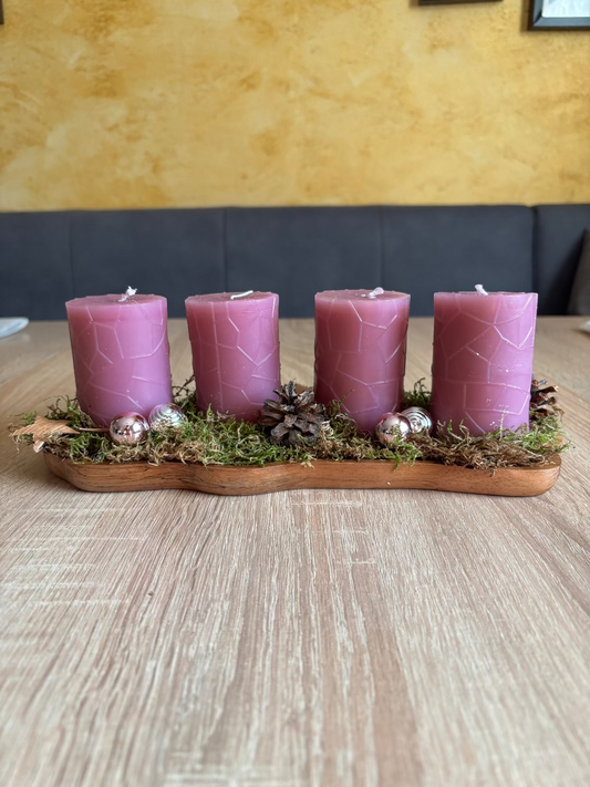 Länglicher Adventskranz mit runden rosa Kerzen, geschmückt mit Moos, Christbaumkugel und Tannenzapfen
