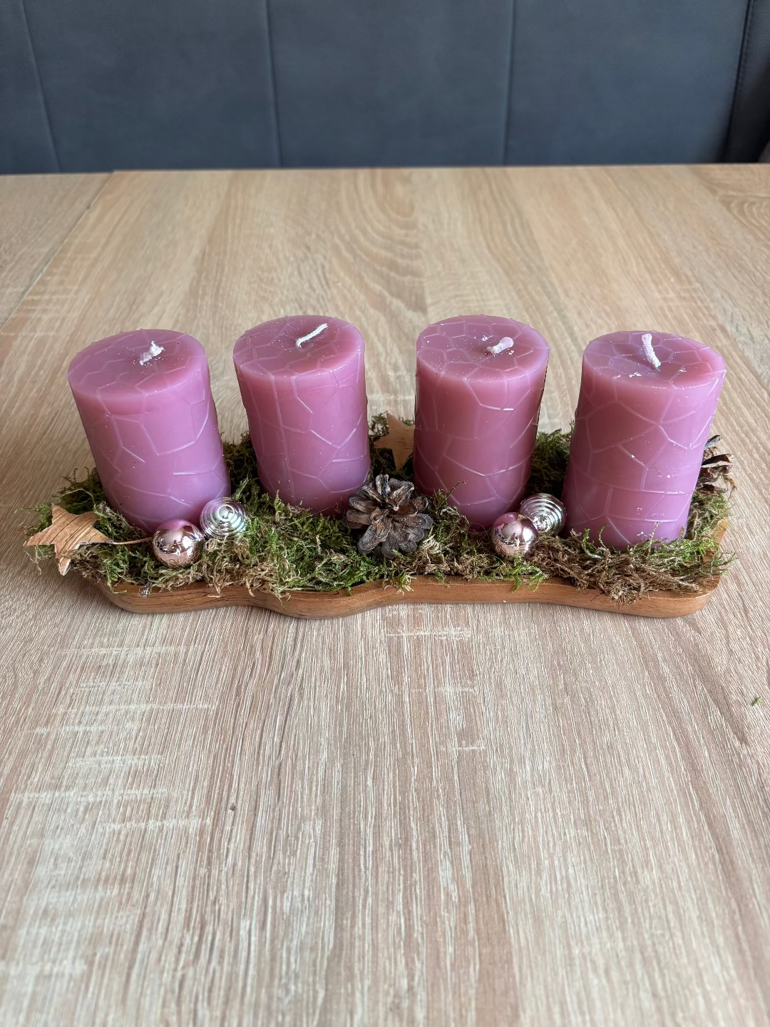 Länglicher Adventskranz mit runden rosa Kerzen, geschmückt mit Moos, Christbaumkugel und Tannenzapfen