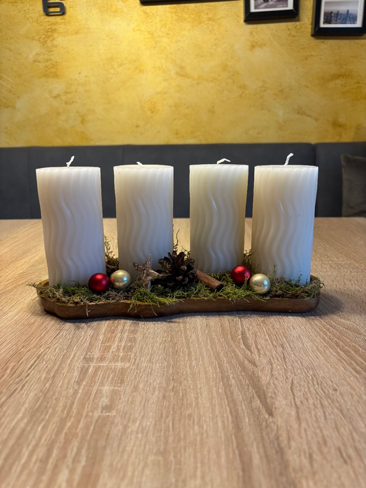 Länglicher Adventskranz mit runden weißen Kerzen, geschmückt mit Moos, Christbaumkugel und Tannenzapfen