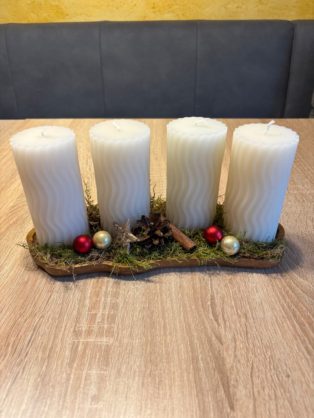 Länglicher Adventskranz mit runden weißen Kerzen, geschmückt mit Moos, Christbaumkugel und Tannenzapfen