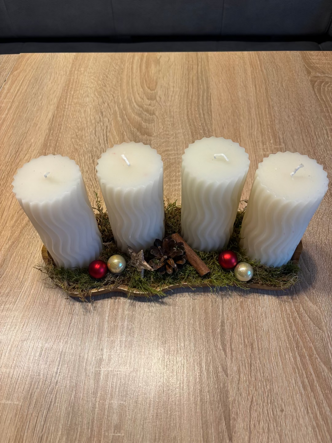 Länglicher Adventskranz mit runden weißen Kerzen, geschmückt mit Moos, Christbaumkugel und Tannenzapfen