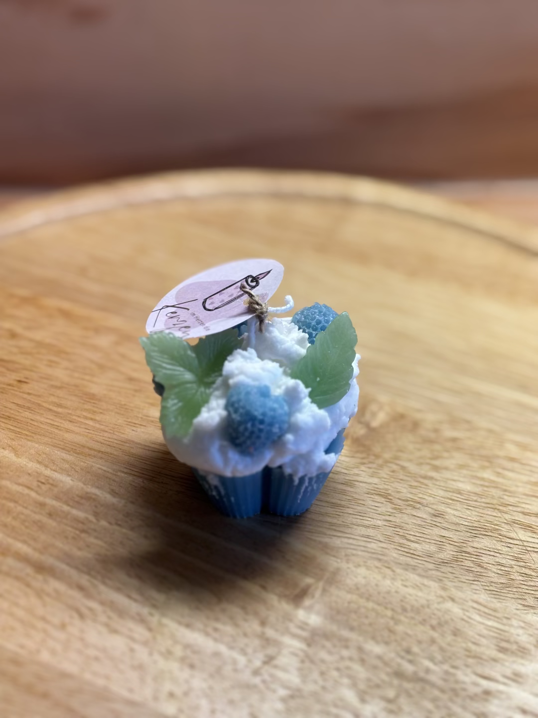 Kerze, die aussieht wie ein blauer Cupcake mit weißer Creme, dekoriert mit Heidelbeeren und Blätter