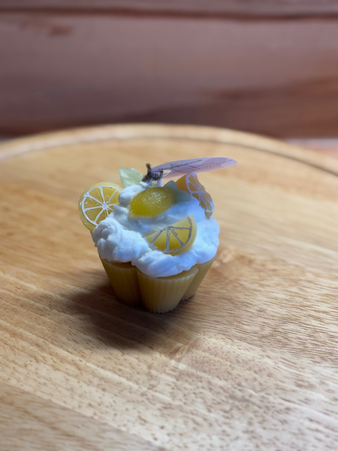 Kerze, die aussieht wie ein gelber Cupcake mit weißer Creme, dekoriert mit Zitronen und Blätter