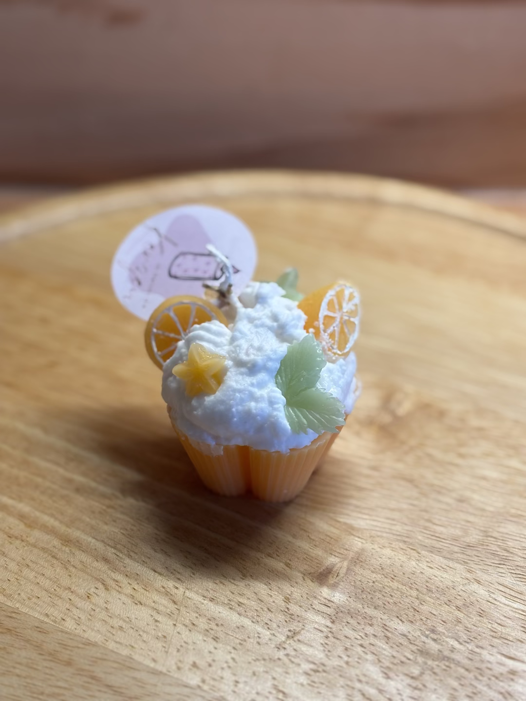 Kerze, die aussieht wie ein oranger Cupcake mit weißer Creme, dekoriert mit Orangen und Blätter