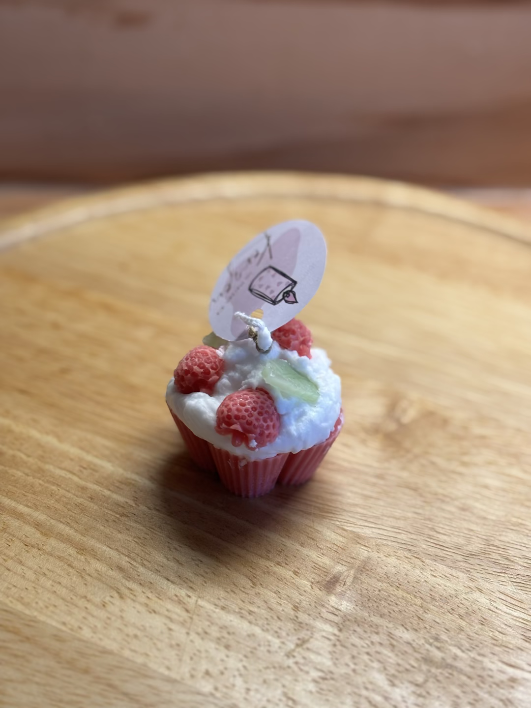 Kerze, die aussieht wie ein roter Cupcake mit weißer Creme, dekoriert mit Erdbeeren und Blätter
