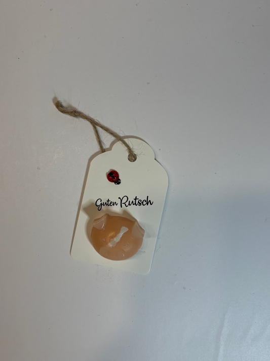 Kerze, die aussieht wie eine Schweinekopf auf einem Blatt Papier, mit Band zum Aufh, worauf "Guten Rutsch" steht und ein kleiner Marienkäfer klebt