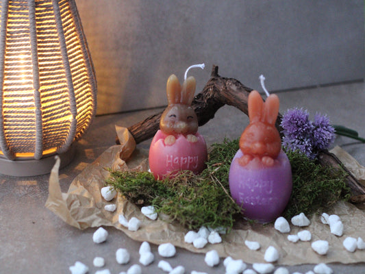 Kerze, wo ein Hase aus einem aufgebrochenen Ei herauslacht. Auf dem Ei steht "Happy Easter" und der Hase sieht glücklich aus