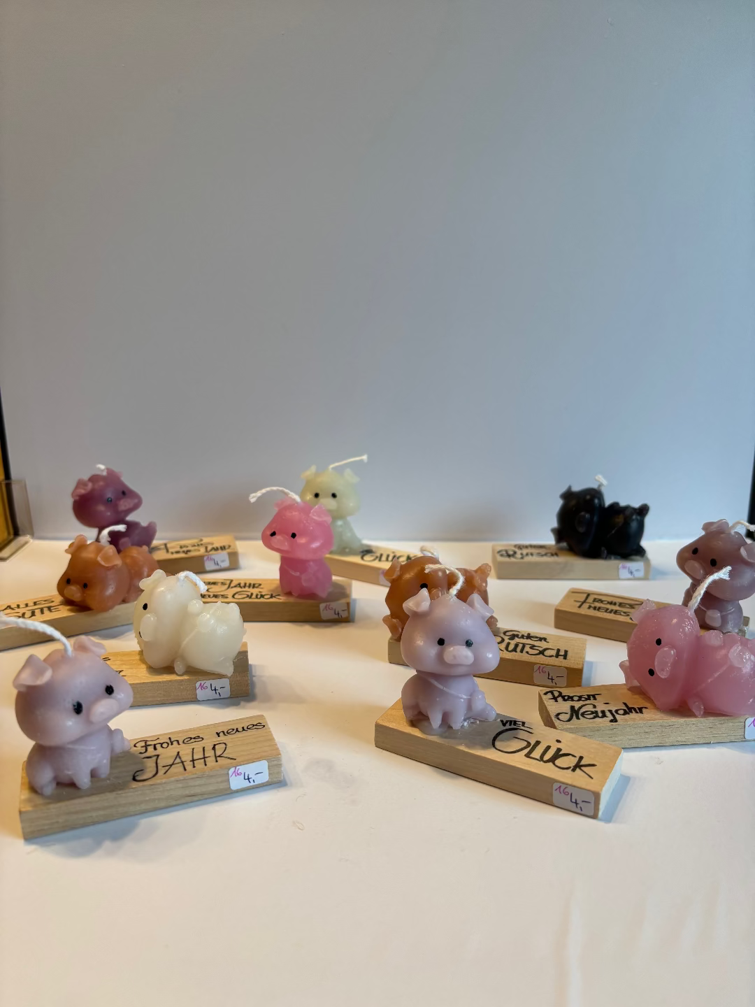 Kerze, die aussieht wie ein kleines Schwein, das entweder sitzt oder liegt und auf einem Brett klebt worauf Glückssprüche für Silvester stehen