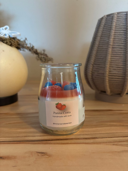 Kerze in einem Glas, die aussieht wie das Dessert Panne Cotta mit Früchten wie Erdbeeren, Heidelbeeren, Himbeeren und Kirschen